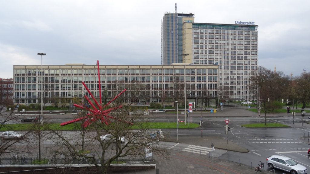 A large building stands behind a striking red sculpture in the foreground, showcasing modern architecture and art.