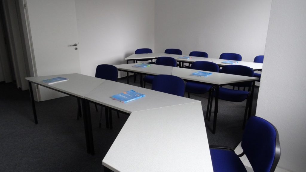 . Interior of a classroom with blue chairs and tables set up for educational purposes.