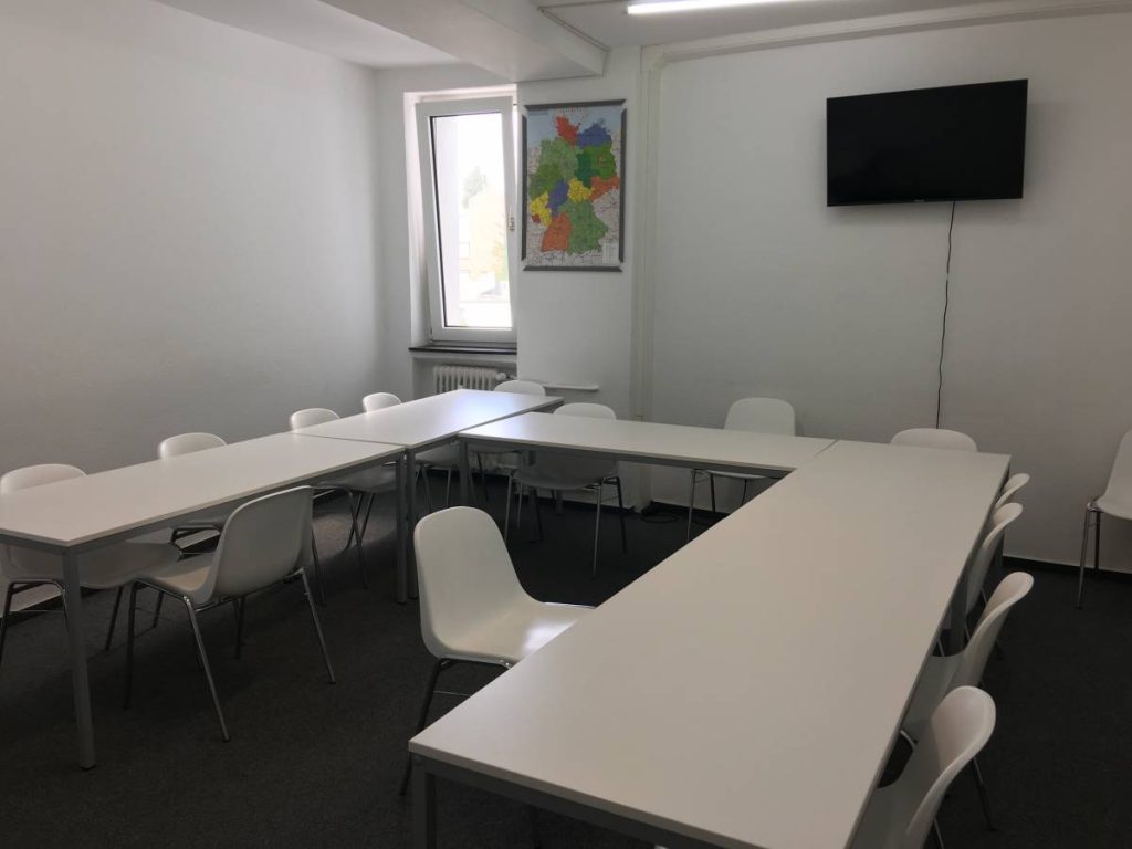  A room featuring white tables and chairs arranged in front of a television.
