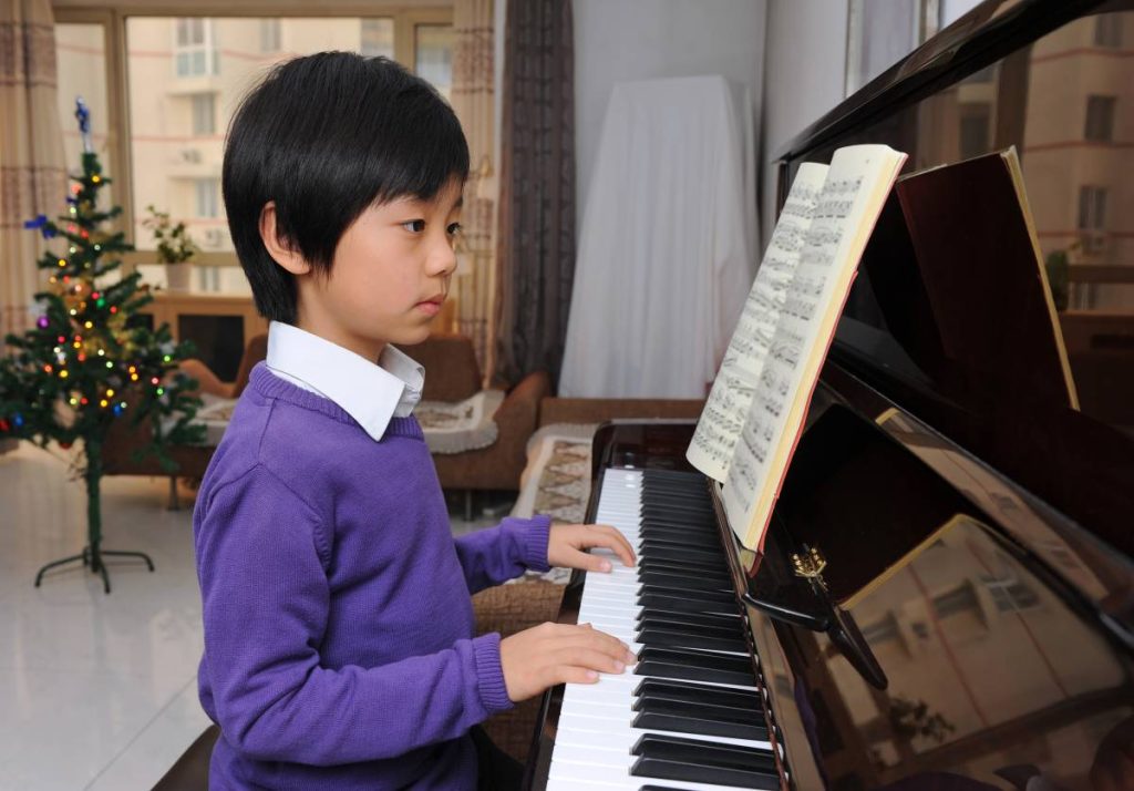 A young boy playing the piano in a cozy living room filled with natural light and colorful decor.